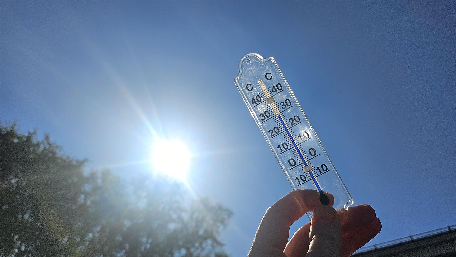 Temperaturmåler holdt opp mot himmelen med klar blå himmel og sol i bakgrunnen
