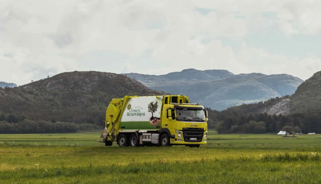 Renovasjonsbil fra Fosen Renovasjon kjører gjennom et grønt landskap med fjell i bakgrunnen.