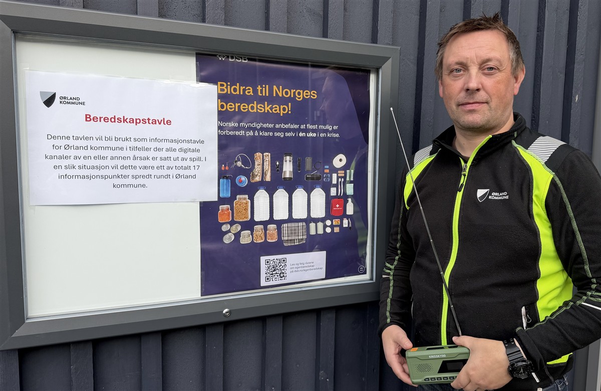Informasjonstavle og en mann som holder en DAB-radio. - Klikk for stort bilde