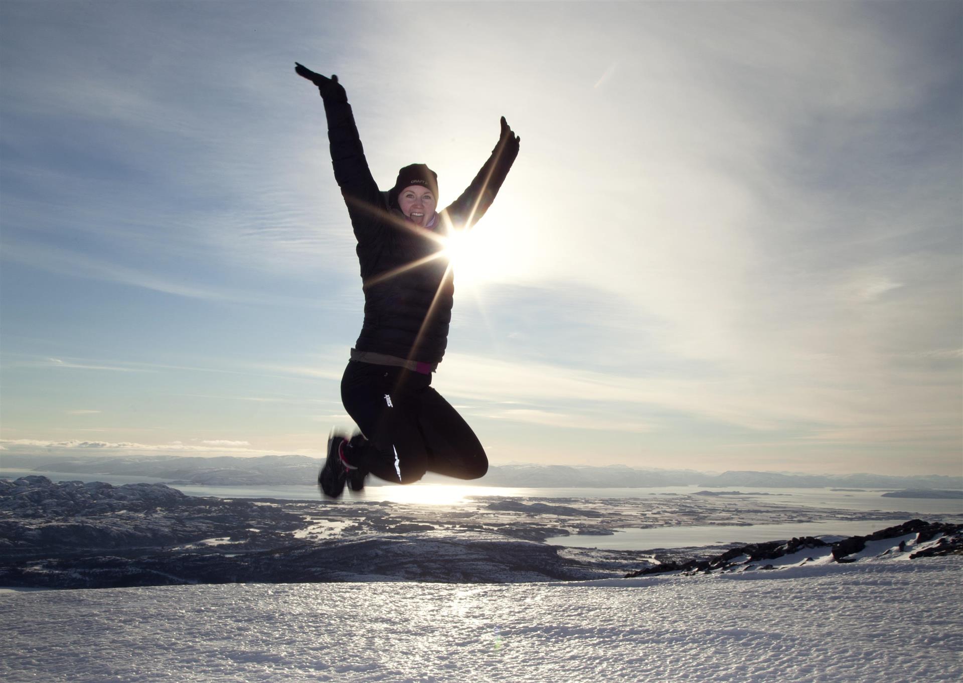Person som hopper. Sol i bakgrunnen. Snø og is. 