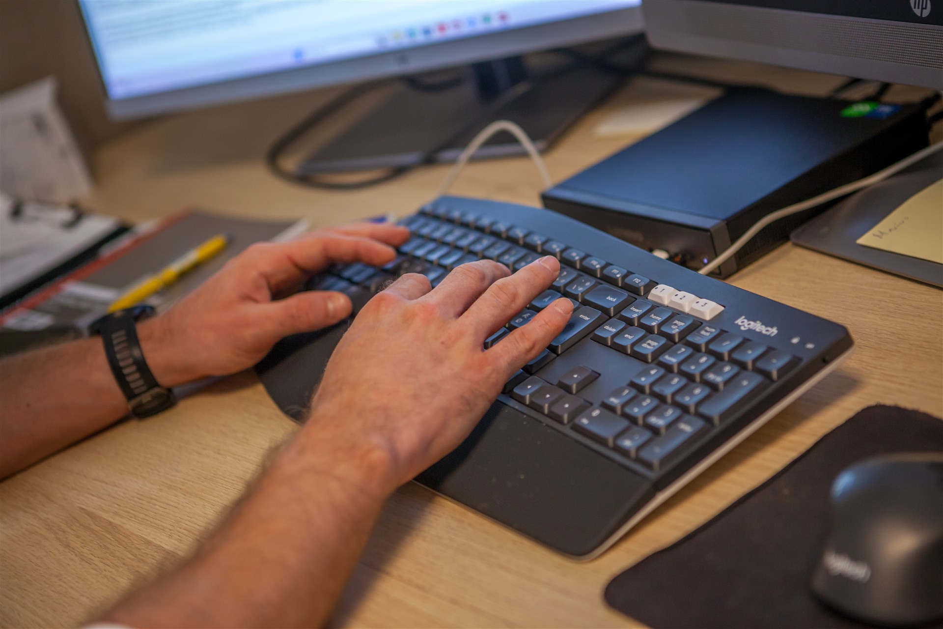 Hender som skriver på et tastatur ved en datamaskin på et kontor.