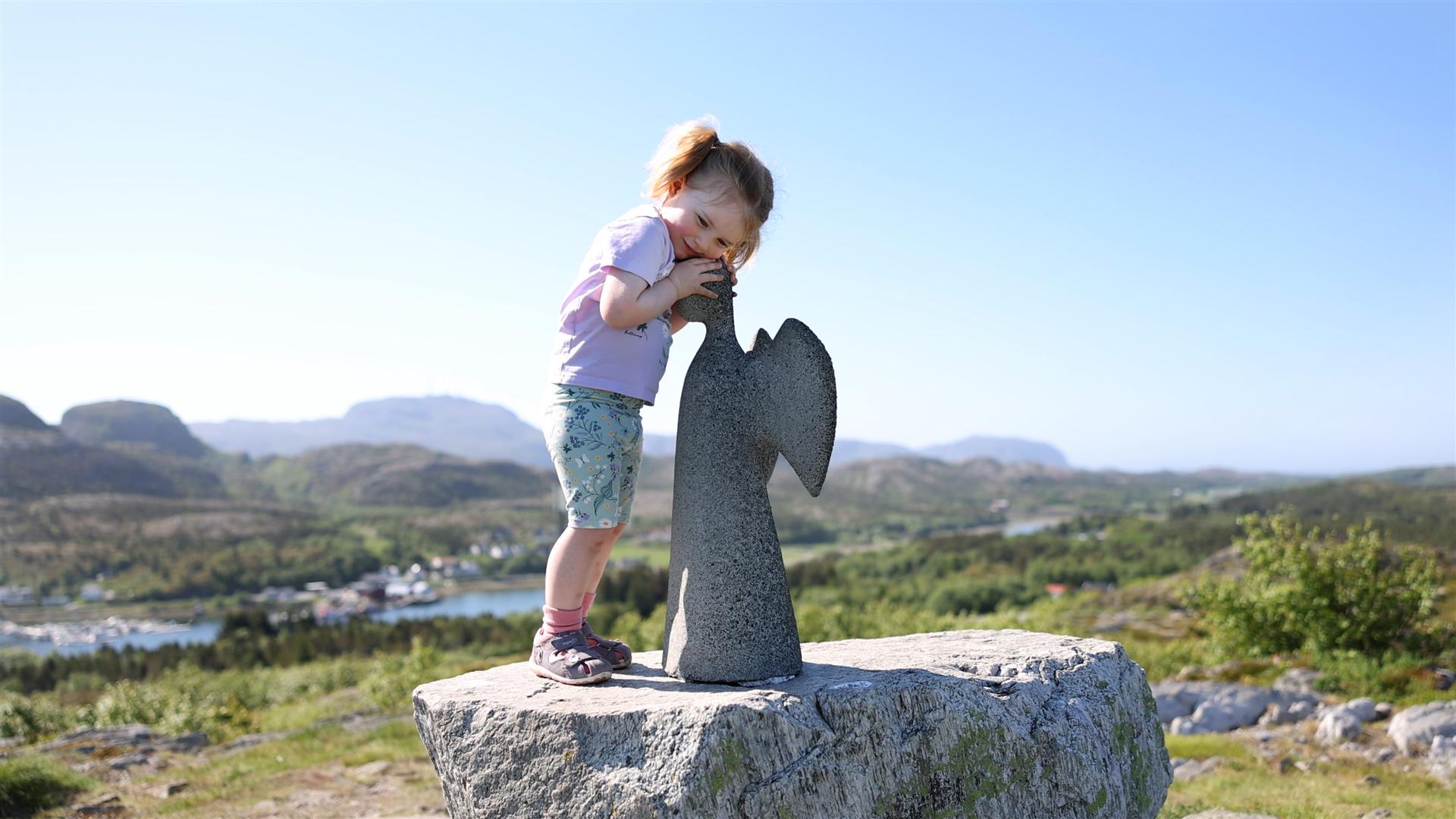 Bilde av jente som står på en stor stein og klemmer Vallersund engelen