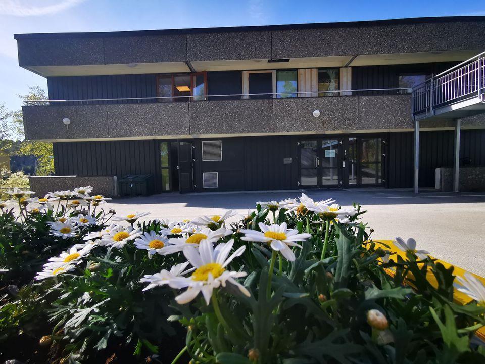 Bilde av et brunt bygg med to etasjer. Blomster i forgrunnen. 