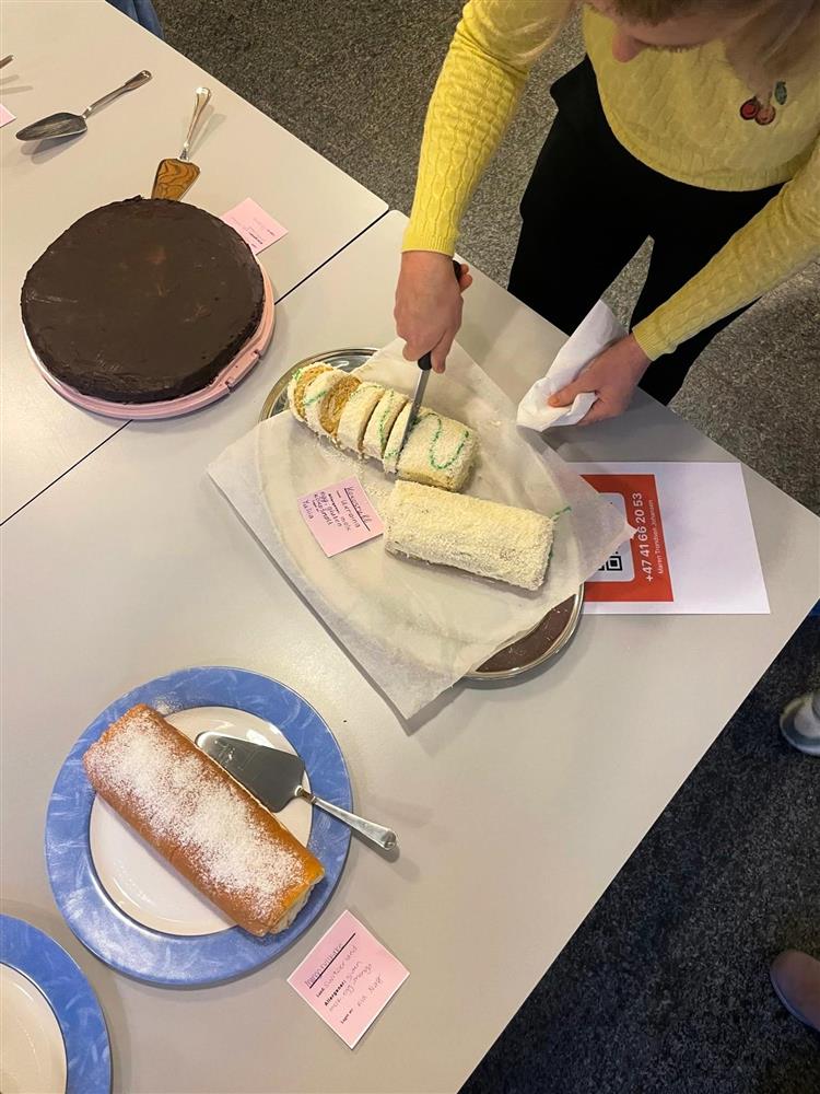 En person forsyner seg fra en hvit rullekake. Ved siden av stå flere andre kaker oppstil.  - Klikk for stort bilde